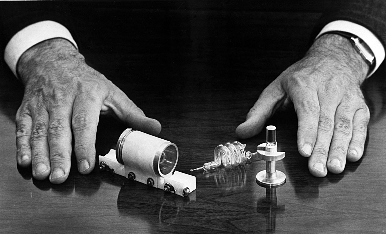 El primer làser de Maiman, desmuntat entre les que segurament són les seues mans, en una imatge de 1987. S’hi pot observar el flaix en forma d’espiral i, a la dreta, el cristall cilíndric de robí. / Hughes Research Laboratories