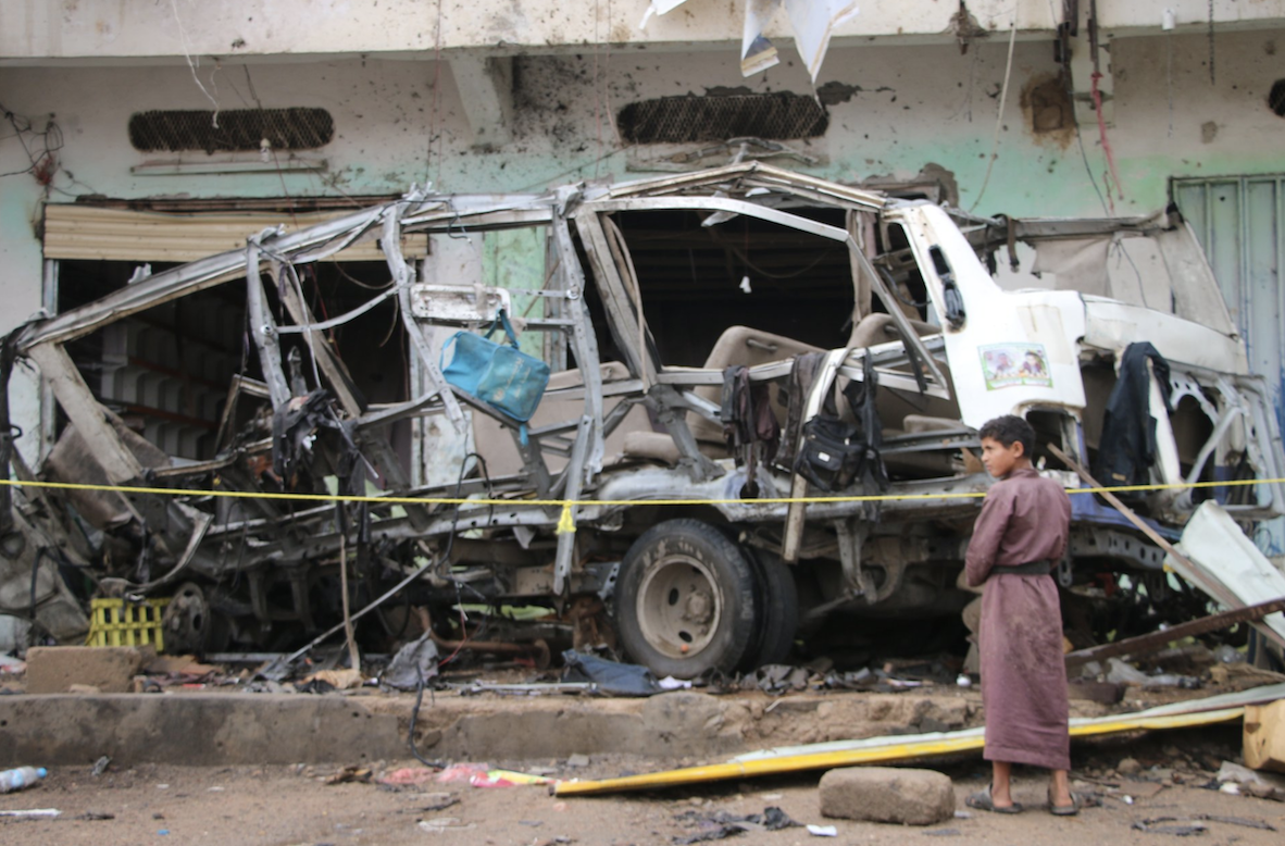 Un nen davant les restes de l'autobus escolar destrossat per un míssil al Iemen (fotografia d'Ahmad Algohbary)