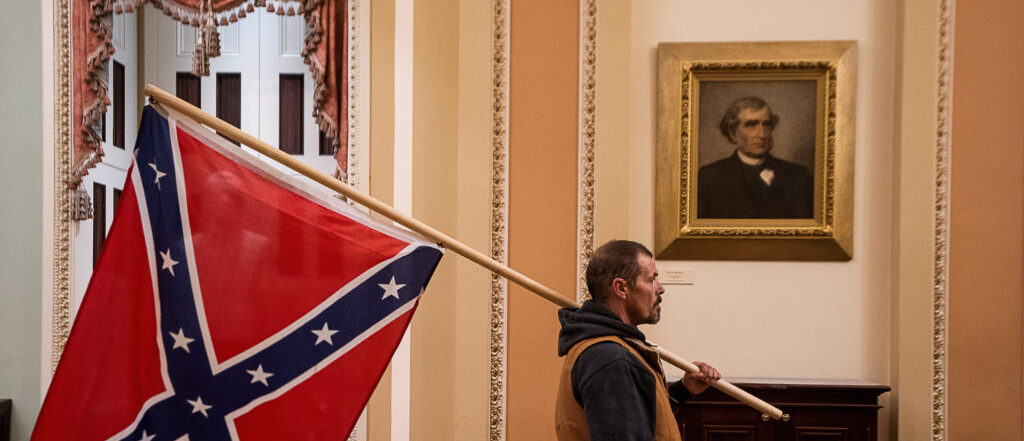 Per primer cop en la història, la bandera confederal entra al Capitoli. A la foto, l'assaltant travessa la sala dels retrats de prohoms de la guerra civil nord-americana contra l'esclavitud que els confederats van perdre.
