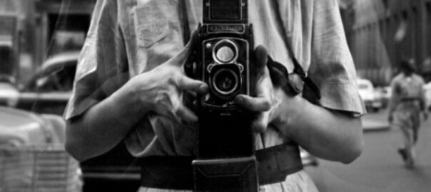 Les mans de Vivian Maier sostenint la seva càmera, sempre a l’alçada de la panxa, per retratar-se reflectida en un vidre.