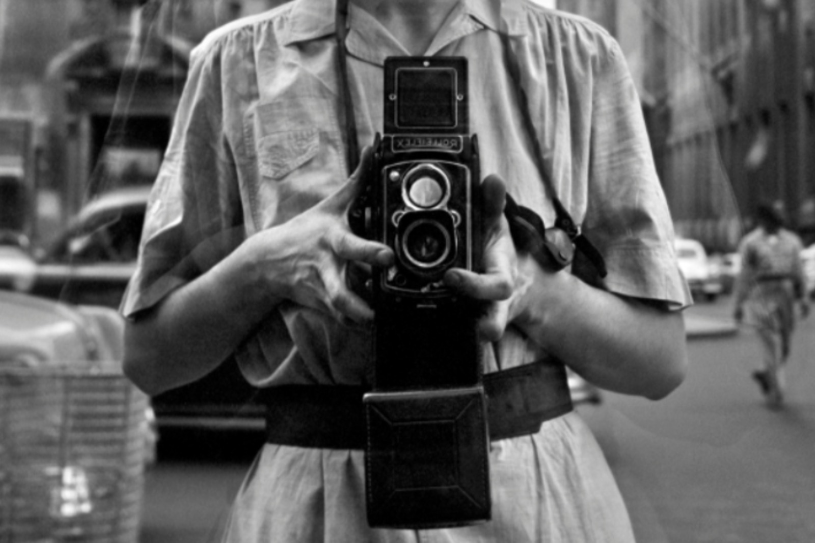 Les mans de Vivian Maier sostenint la seva càmera, sempre a l’alçada de la panxa, per retratar-se reflectida en un vidre.