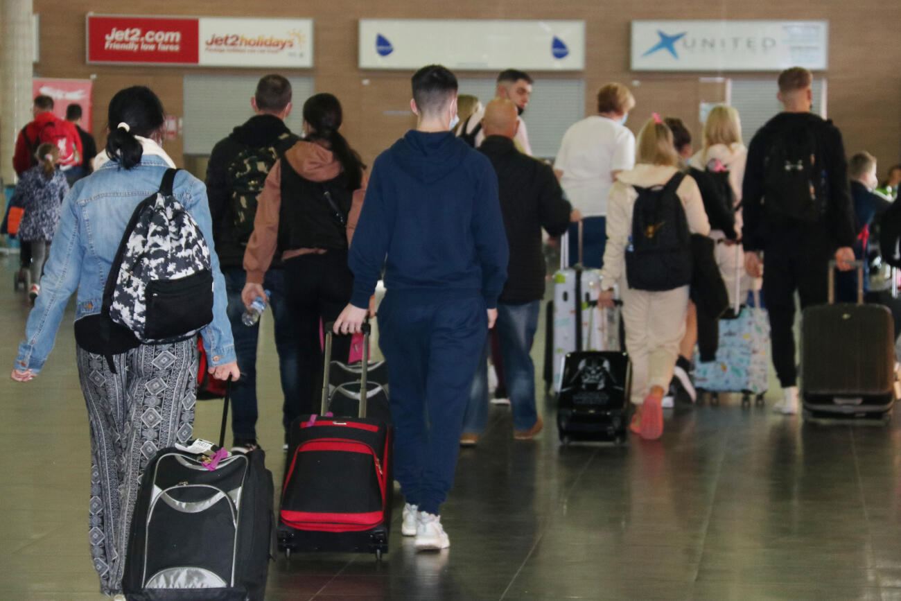 Passatgers carregats de maletes, caminant, d'esquena, a la terminal de l'aeroport de Reus (Fotografia: ACN).