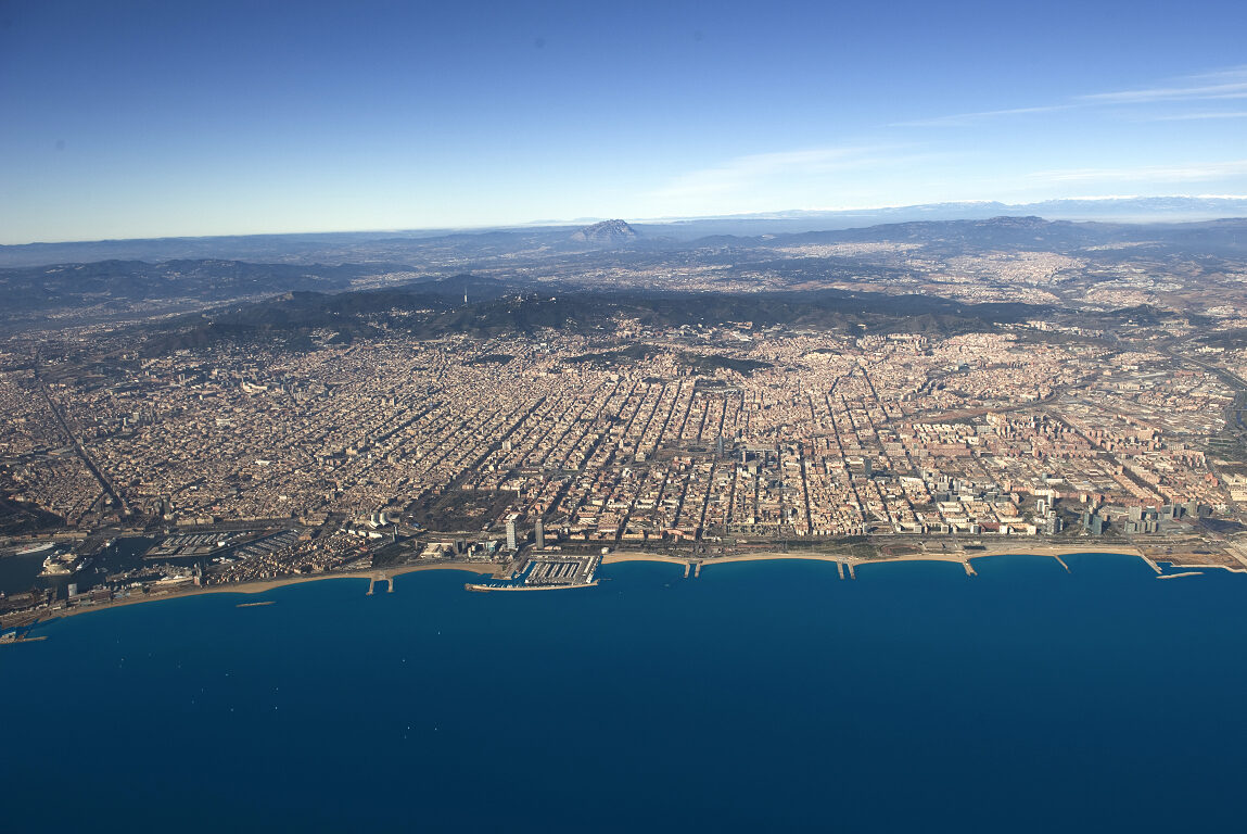 Vista aèria des del mar de la ciutat de Barcelona, entre Montjuïc i el riu Besòs. Enfront la serralada de Collserola i en el fons la muntanya de Montserrat i Sant Llorenç del Munt i l'Obac.