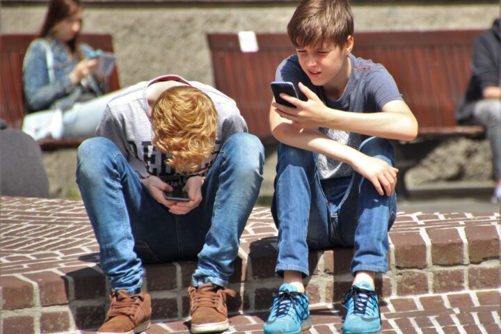 Dos adolescents consulten el telèfon mòbil al carrer.
