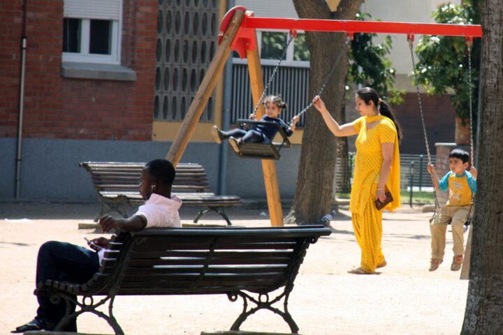 Una dona hindú gronxa a uns nens un parc de Vic, mentre un home subsaharià escolta música en un banc. (fotografia d'arxiu)