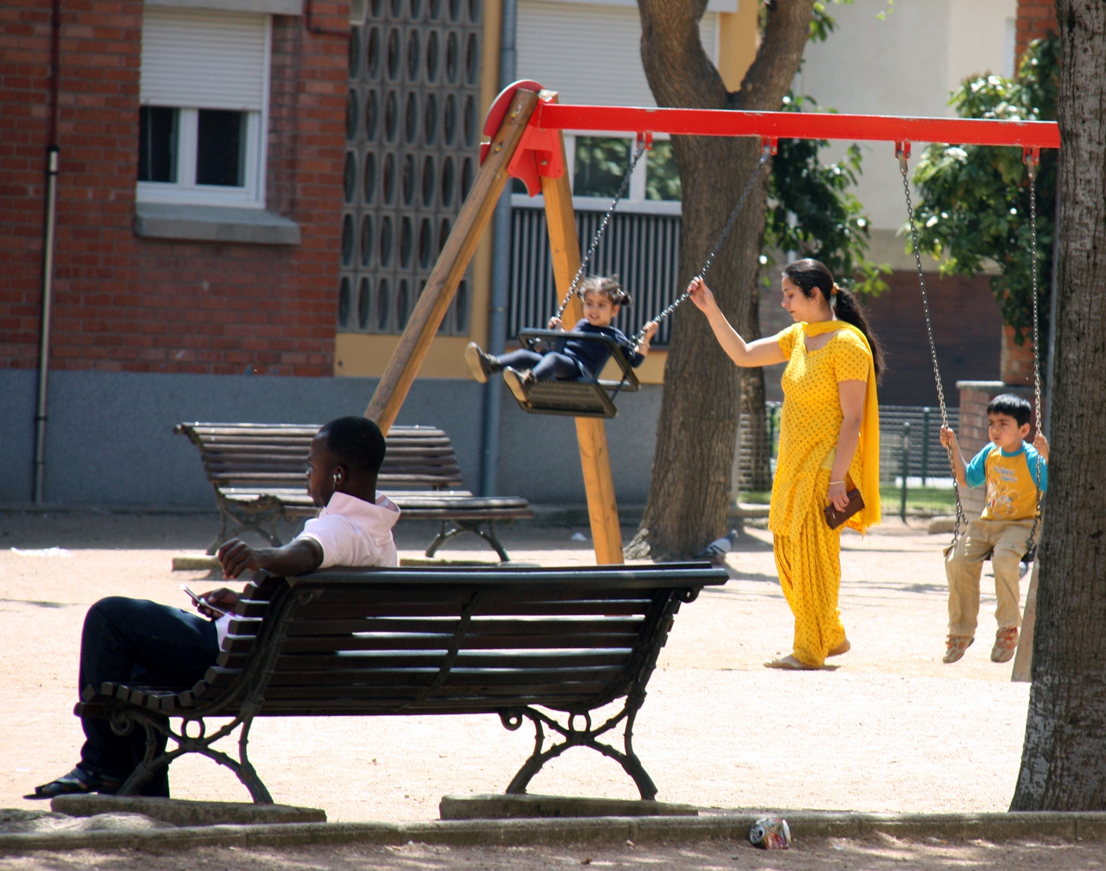 Una dona hindú gronxa a uns nens un parc de Vic, mentre un home subsaharià escolta música en un banc. (fotografia d'arxiu)