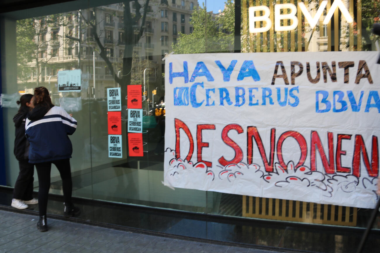 Dues activistes enganxant cartells a la façana de l'oficina del BBVA (fotografia: ACN).