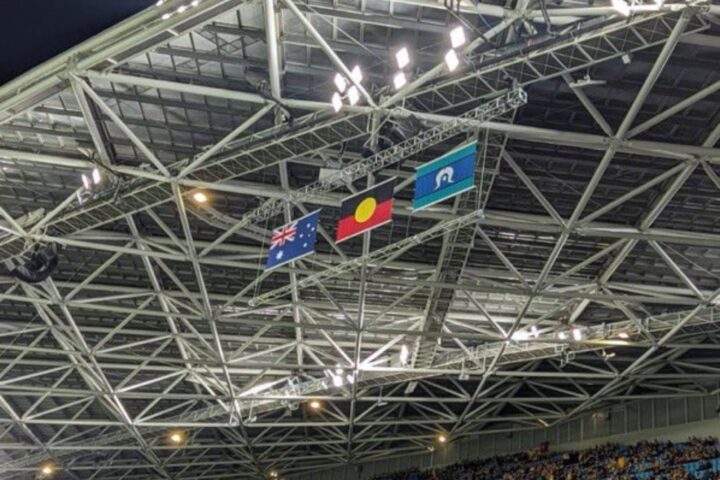 La Bandera nacional australiana (esquerra), la bandera aborigen australiana (centre) i la bandera de les illes de l'estret de Torres (dreta) onegen en un estadi
