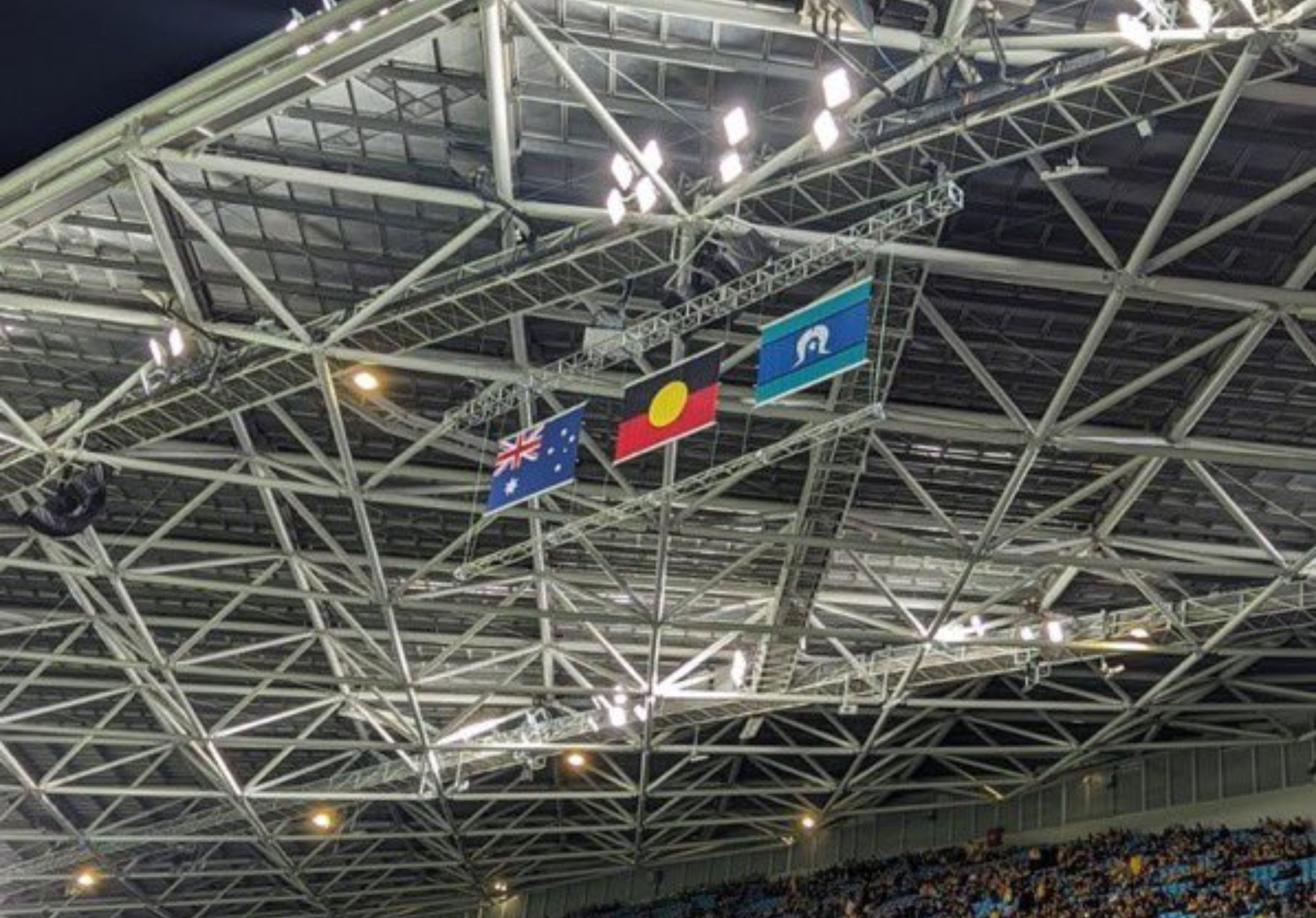 La Bandera nacional australiana (esquerra), la bandera aborigen australiana (centre) i la bandera de les illes de l'estret de Torres (dreta) onegen en un estadi