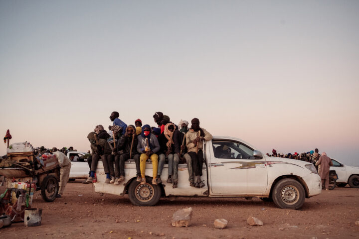 Un camió destrossat aparcat a la vora d'Agadez, amb un grup de migrants esperant fer el camí cap a la frontera amb Líbia, a tres dies en cotxe des de la ciutat. (Guy Peterson per a The Washington Post)