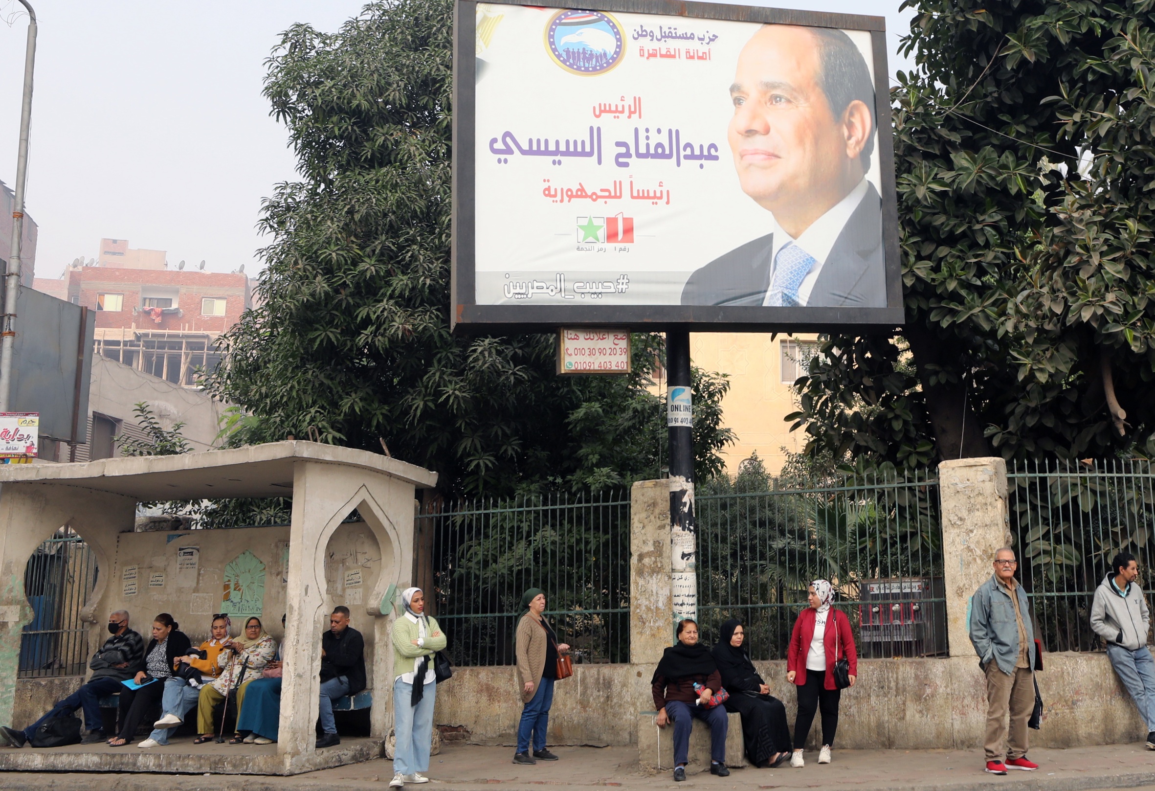 Vianants esperen el bus sota un cartell electoral d'al-Sisi al Caire (fotografia: Khaled Elfiqi/EFE)