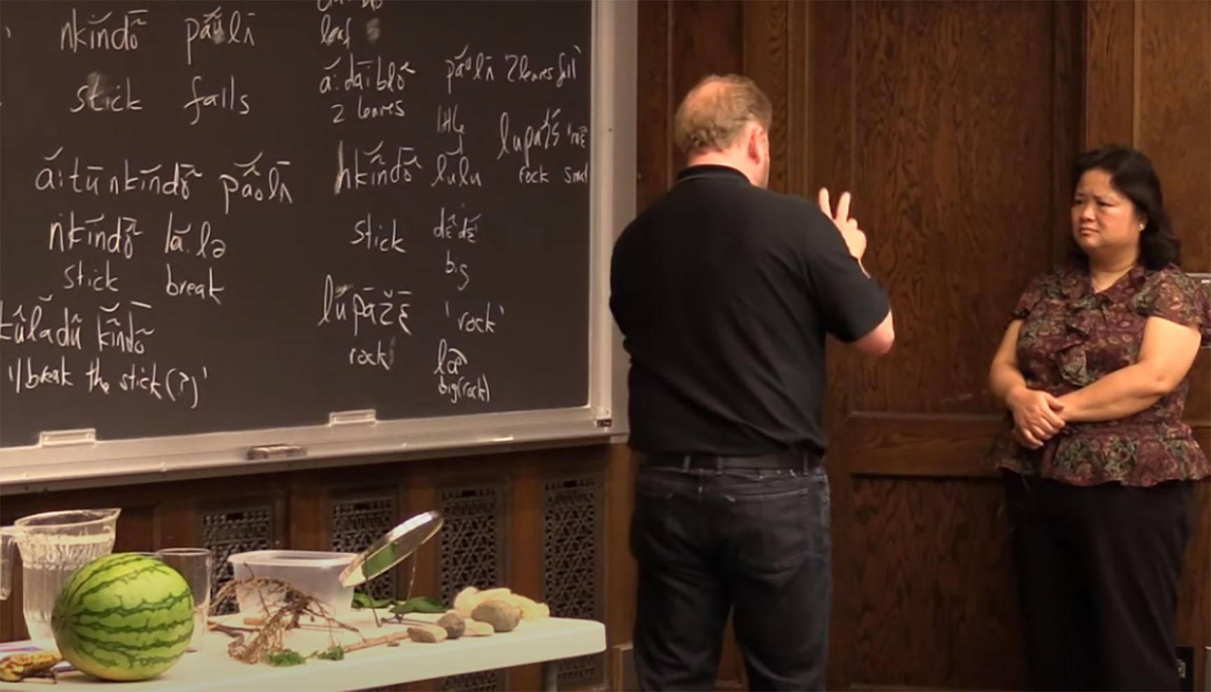 Demostració de treball de camp monolingüe amb una parlant de la llengua hmong i el lingüista Daniel Everett. En la imatge es veu la taula amb els objectes utilitzats, i la pissarra amb anotacions i alguns intents de traducció a l’anglès.