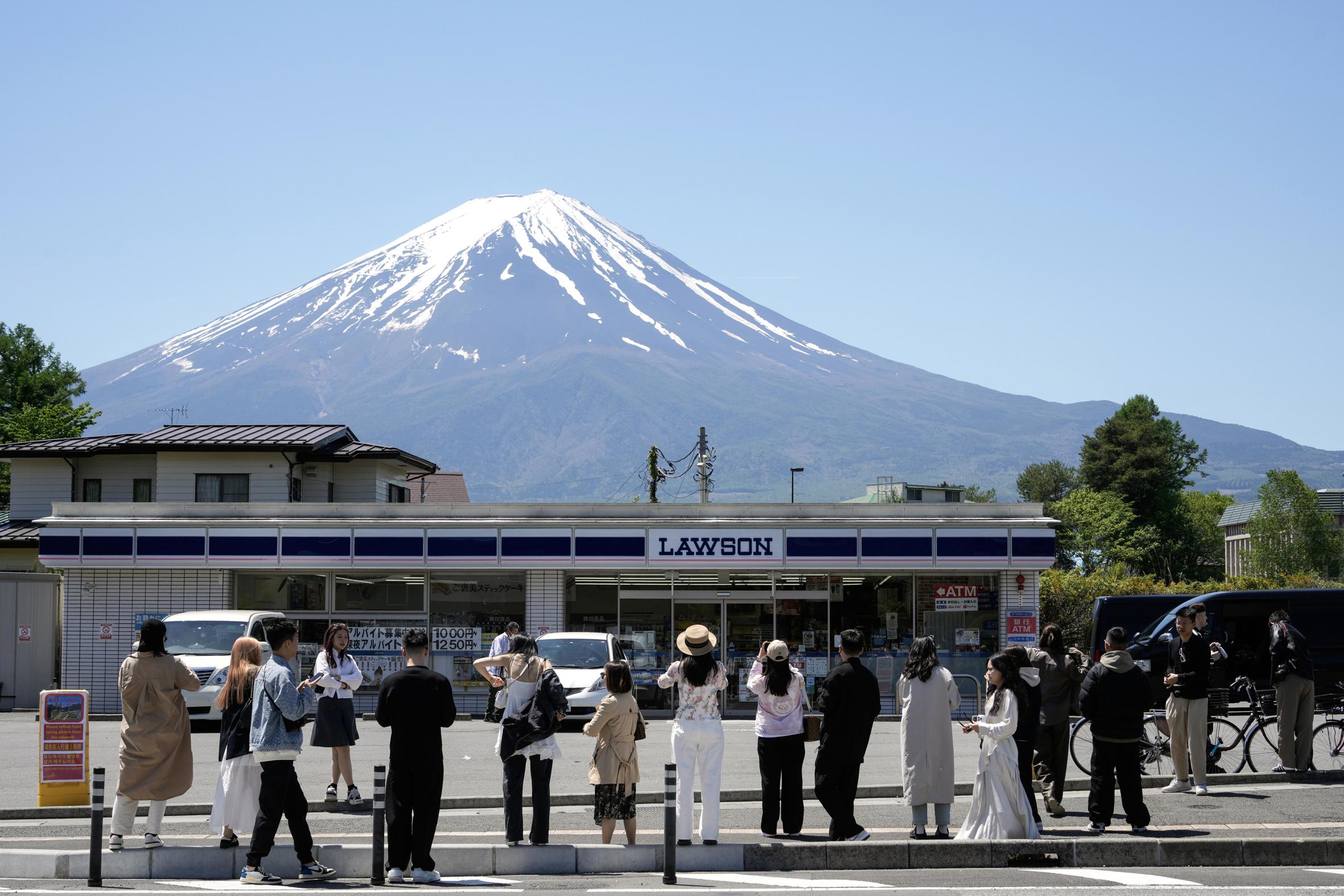 Un grup de turistes fa fotografies a la botiga Lawson de Fujikawaguchiko, amb el mont Fuji de fons (fotografia: Franck Robichon/EFE)