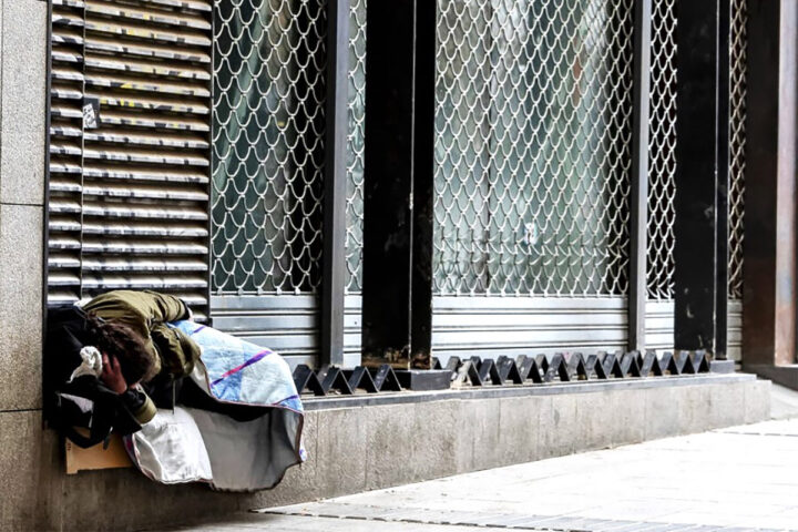 Una persona sense-sostre dorm al carrer encara que sigui a sobre d’arquitectura hostil, Barcelona, 20.2.2024 (fotografia: Albert Salamé).