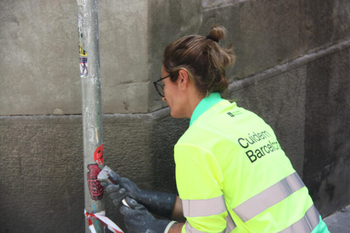 Una treballadora de l'Ajuntament treu adhesius de la via pública.