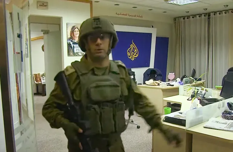 Un soldat israelià a les oficines d'Aljazeera a Ramal·lah. Darrere seu, una fotografia de la periodista de la cadena Shireen Abu Akleh, assassinada per l'exèrcit israelià.