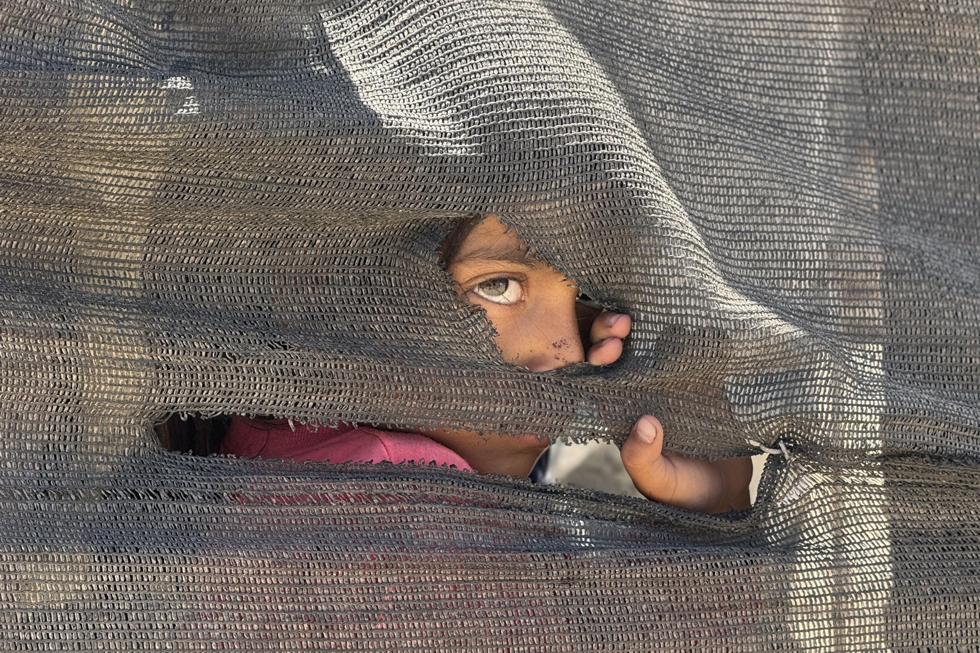 Una xiqueta mira darrere una parada improvisada al port de la ciutat de Gaza, on milers de desplaçats pels atacs israelians han trobat refugi, dimarts (fotografia: Ahmad Awad).