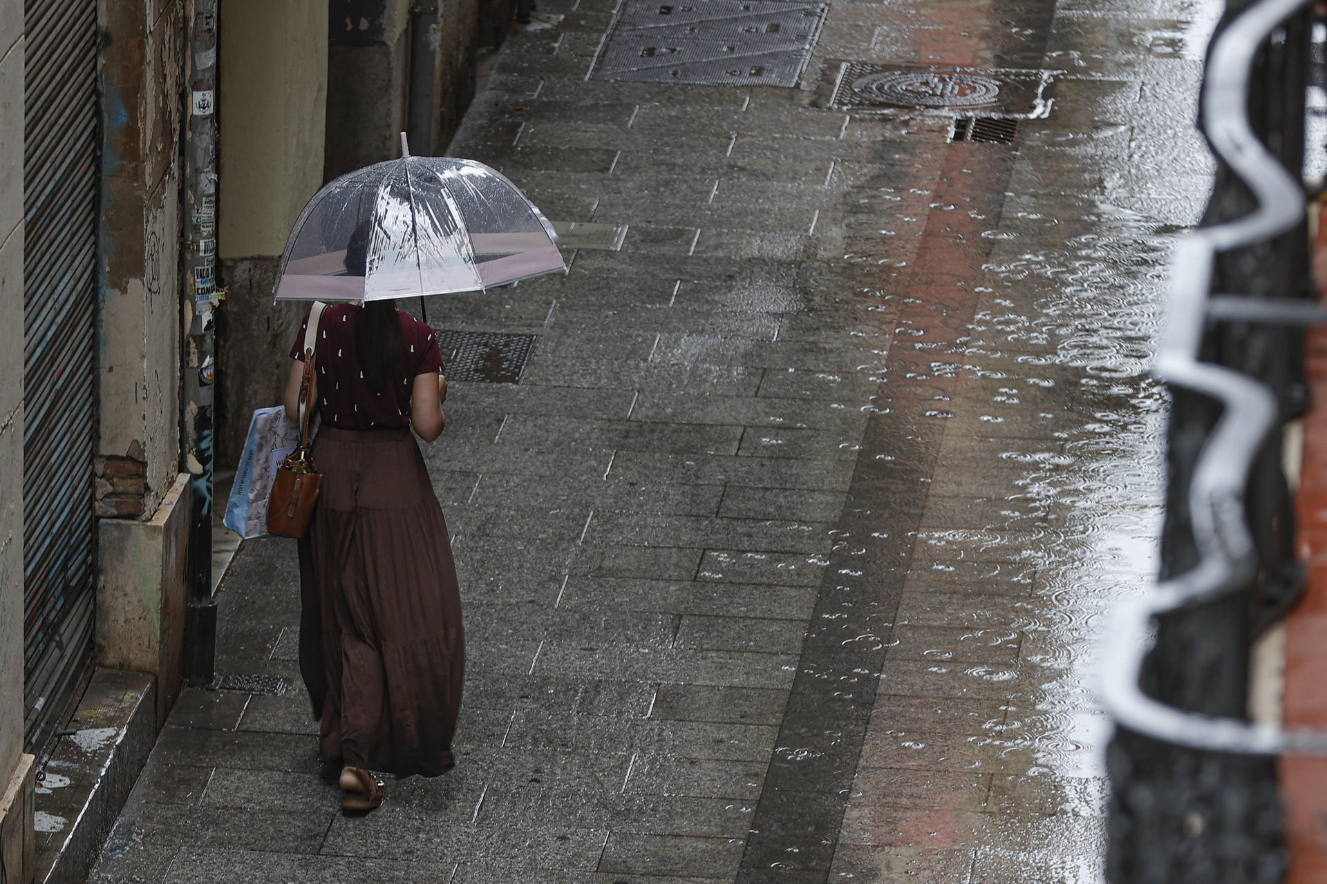Una dona camina sota la pluja a un carrer de València. Fotografia: EFE/Manuel Bruque