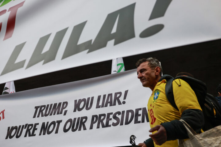 Un manifestant, vestit amb una samarreta de la selecció de futbol brasilera, passa per davant de dos cartells en què es llegeix 