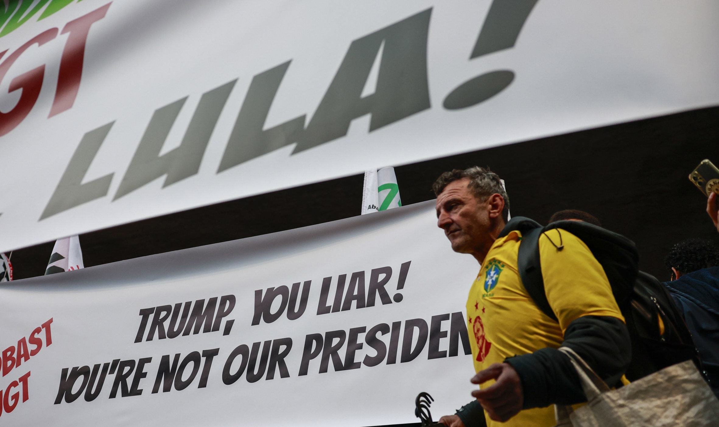 Un manifestant, vestit amb una samarreta de la selecció de futbol brasilera, passa per davant de dos cartells en què es llegeix 