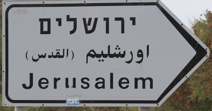 Un cartell israelià disminuint el nom àrab de la ciutat i donant preminència a la transliteració en alfabet àrab del nom jueu de la ciutat