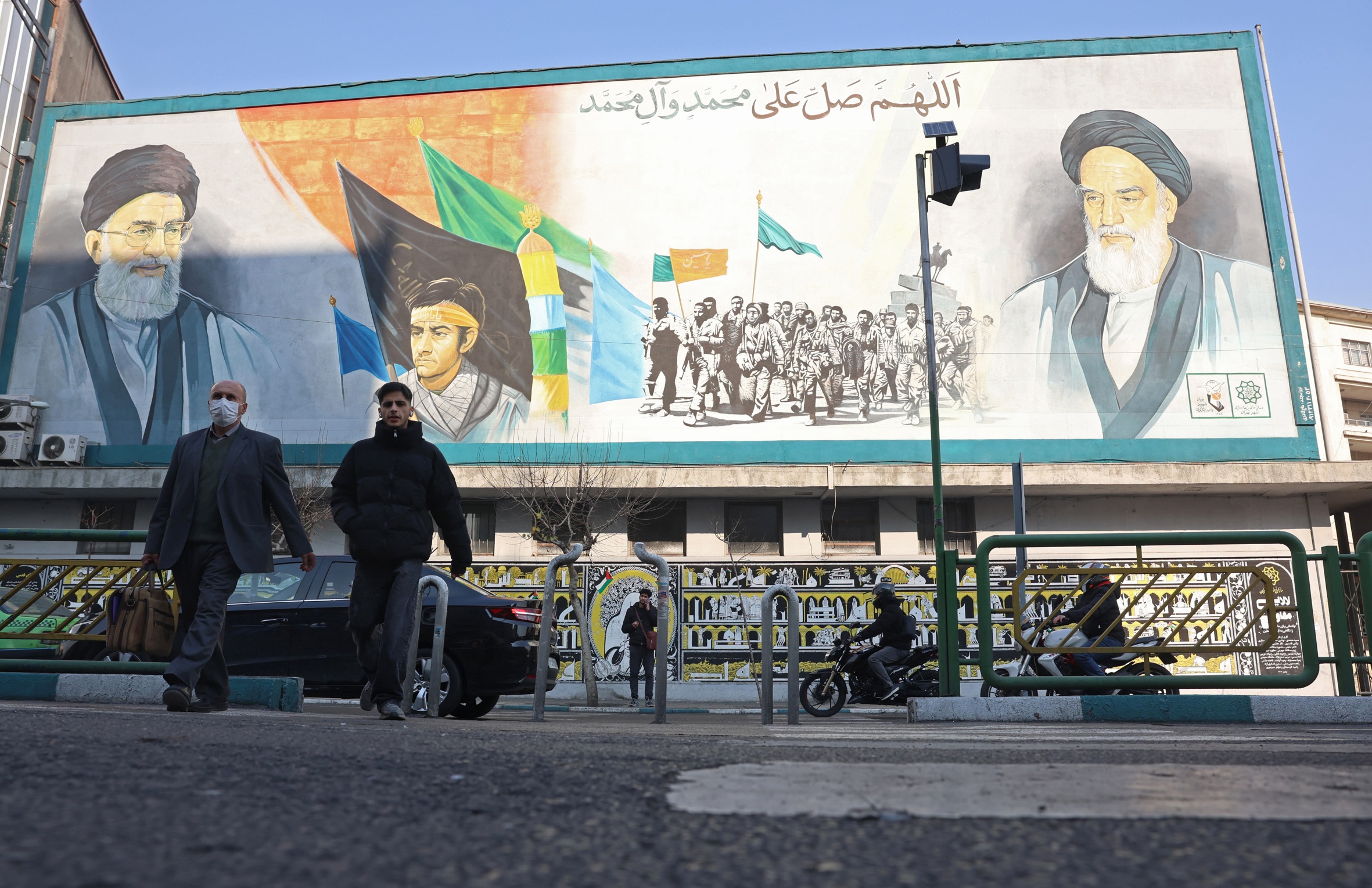 Dos vianants passen per davant d'un mural amb el rostre del líder suprem de l'Iran, l'aiatol·là Ali Khamenei, en un carrer de Teheran, la capital del país, aquesta setmana (fotografia: Abedin Taherkenareh/Efe).