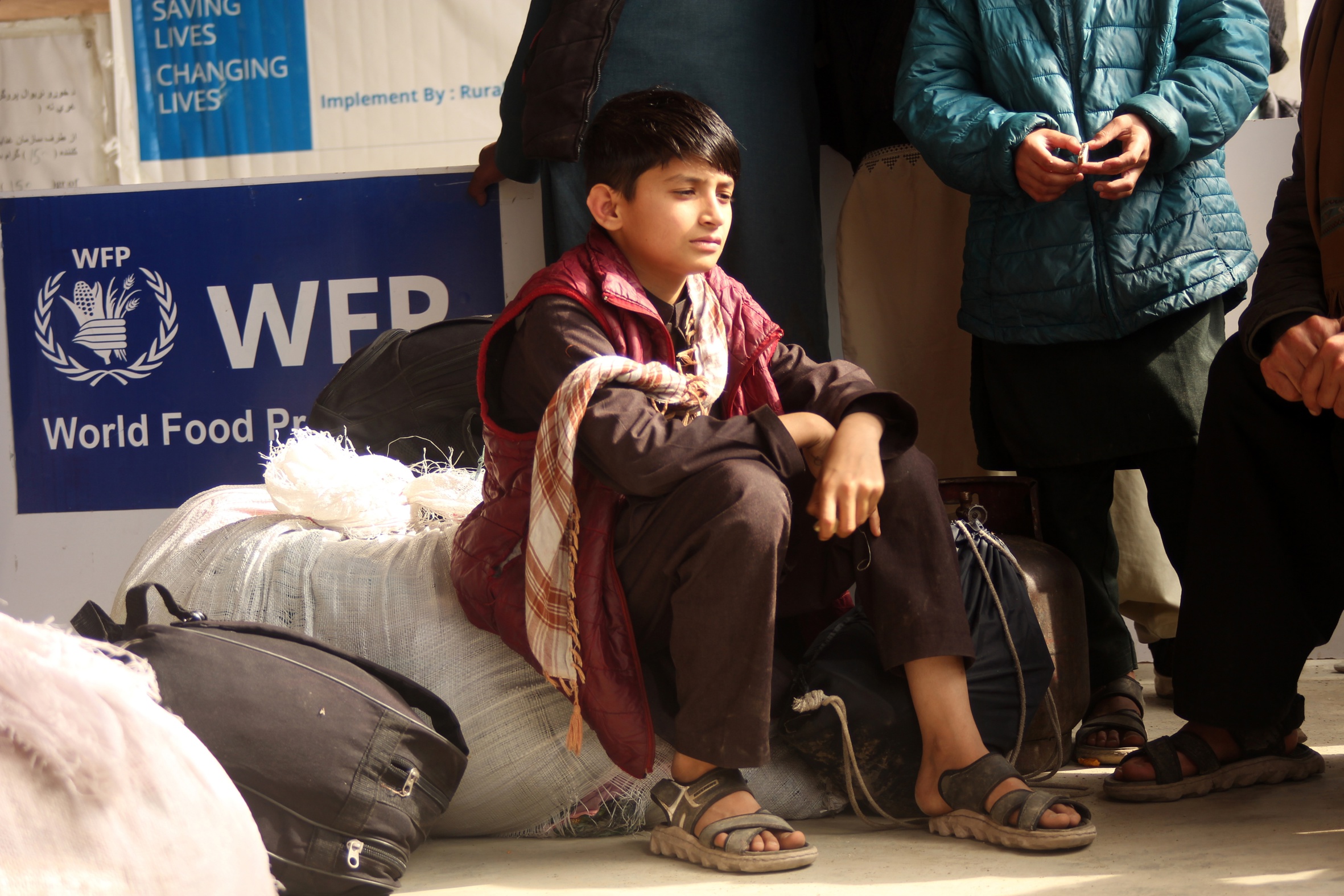 Un infant afganès seu davant un cartell amb el logotip del Programa Mundial d'Aliments de l'ONU (PMA) a Torkham, a la frontera entre el Paquistan i l'Afganistan, la setmana passada (fotografia: Stringer/Efe).